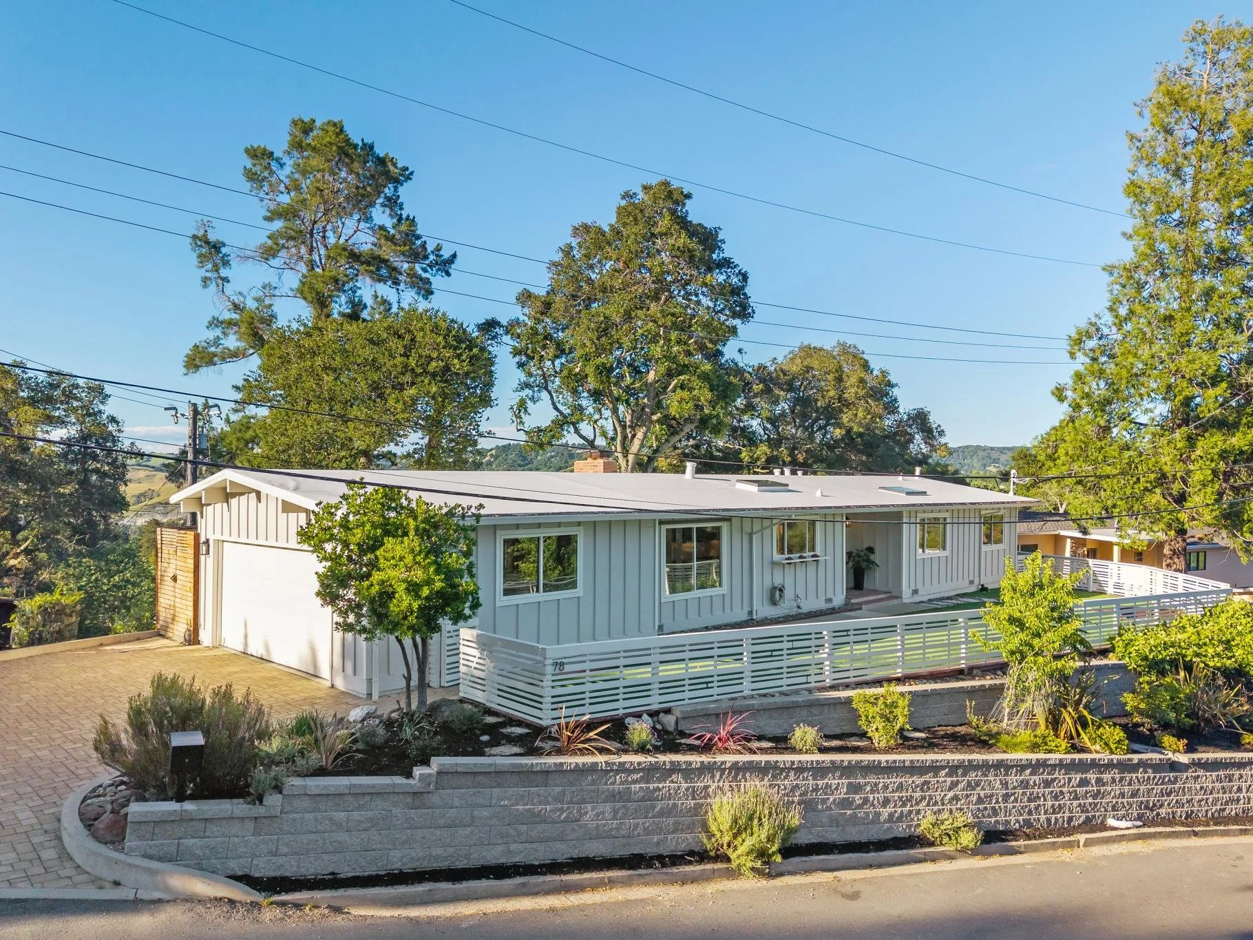 A white modern house with a fenced porch, surrounded by trees, on a sunny day.