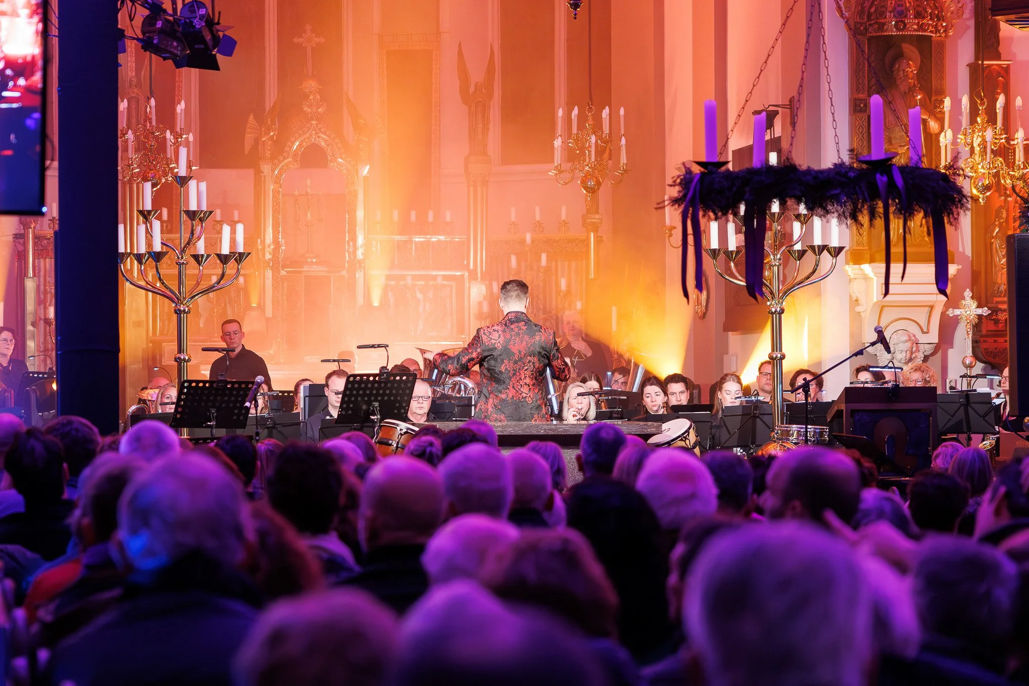 Gezichtspunt op een concert of orkest in een kerkzaal met bizarre verlichting en decoraties, waaronder kandelaars en kleurrijk licht.