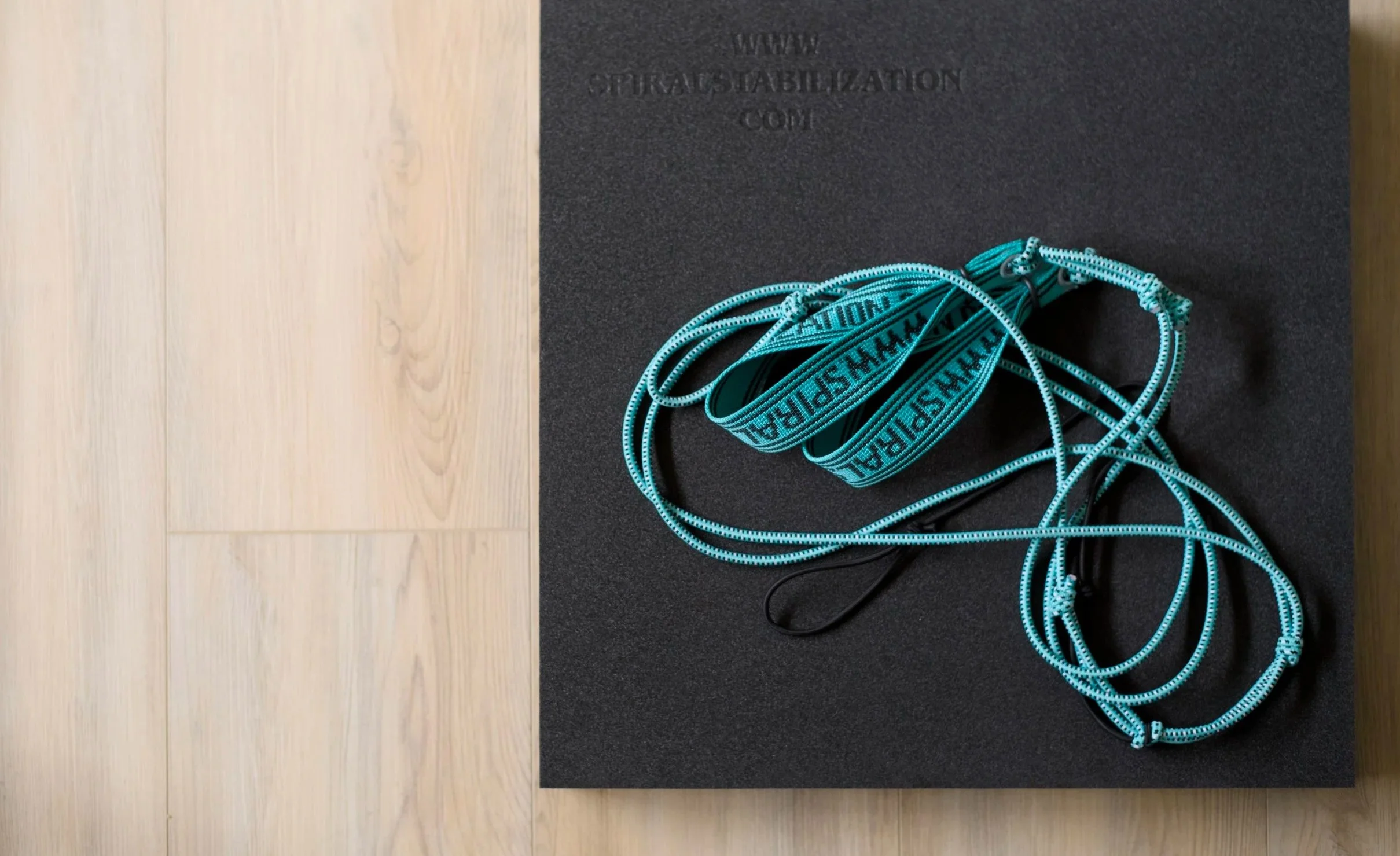 Blue harness with black straps on a black foam mat placed on a light wooden floor.