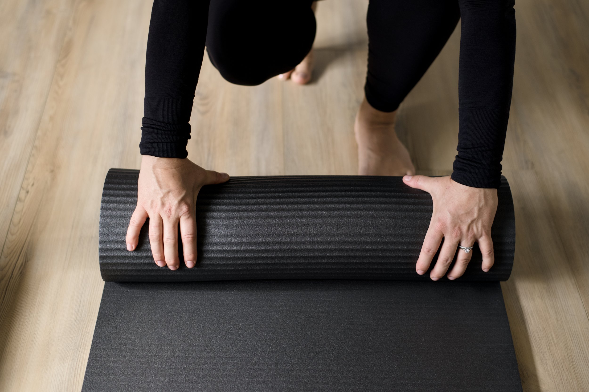 Person rolling out a black yoga mat on wooden floor.