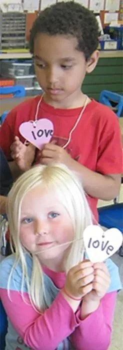 Two children show off their heart word necklaces, a word they can read and write