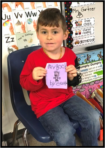 A young boy  shows off a book he wrote and illustrated