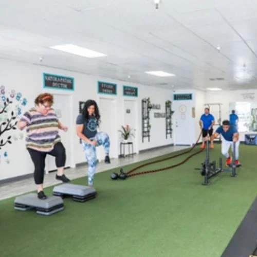 People exercising with step platforms, battle ropes, and workout equipment in a gym.