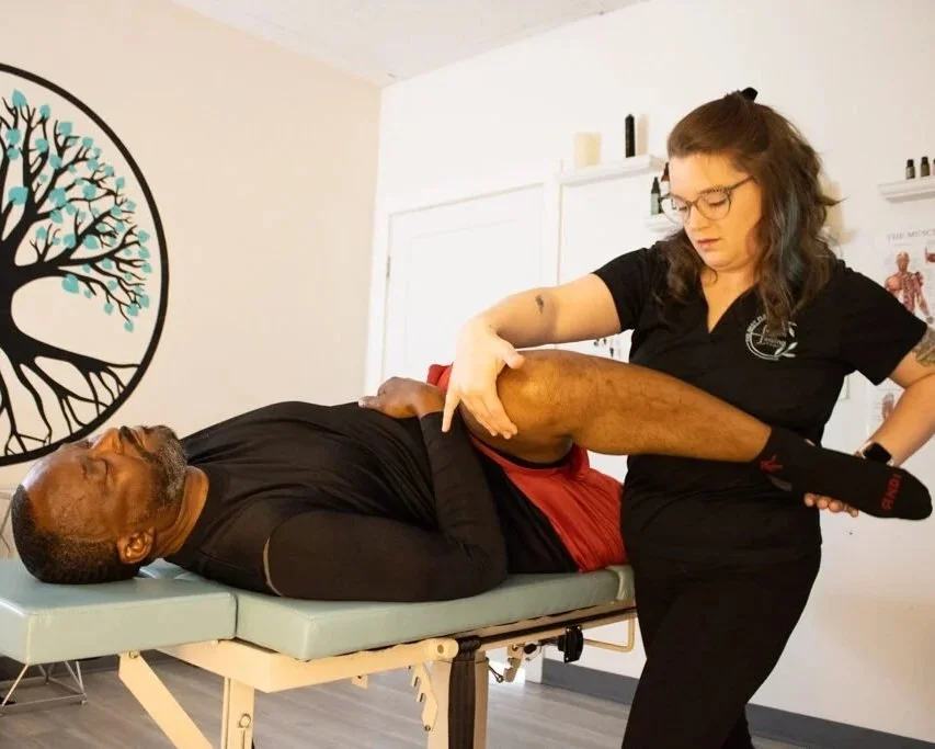 A woman performing physical therapy or massage on a man lying on a treatment table in a clinic or therapy room.
