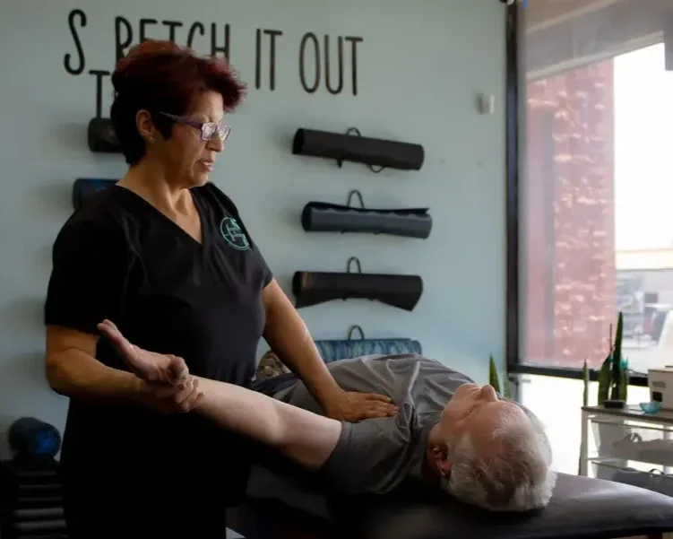 A chiropractor or massage therapist performing a spinal adjustment or massage on an elderly man lying face down on a treatment table.