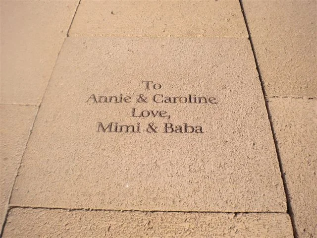 A sidewalk engraved with a message that reads, 'To Annie & Caroline, Love, Mimi & Baba'.