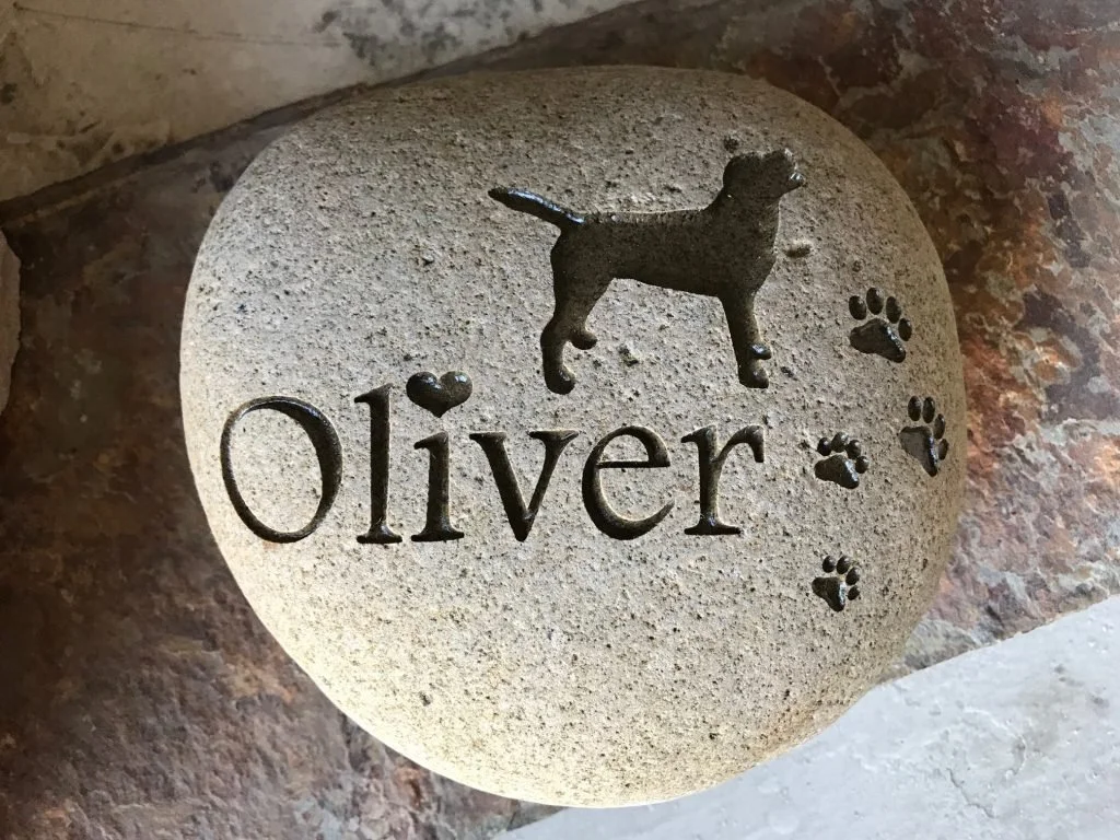 A decorative stone with the name 'Oliver' engraved on it, accompanied by a silhouette of a dog and paw prints.