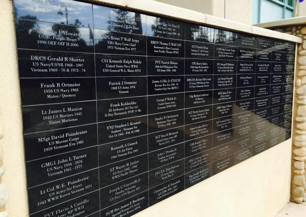 A memorial wall with black engraved plaques honoring deceased military personnel.