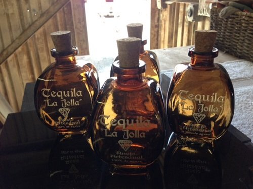 Four amber glass bottles of tequila with cork stoppers on a black surface.