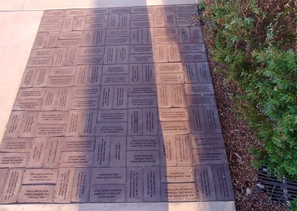 A memorial sidewalk with engraved bricks honoring fallen soldiers, placed next to a grassy area with bushes.