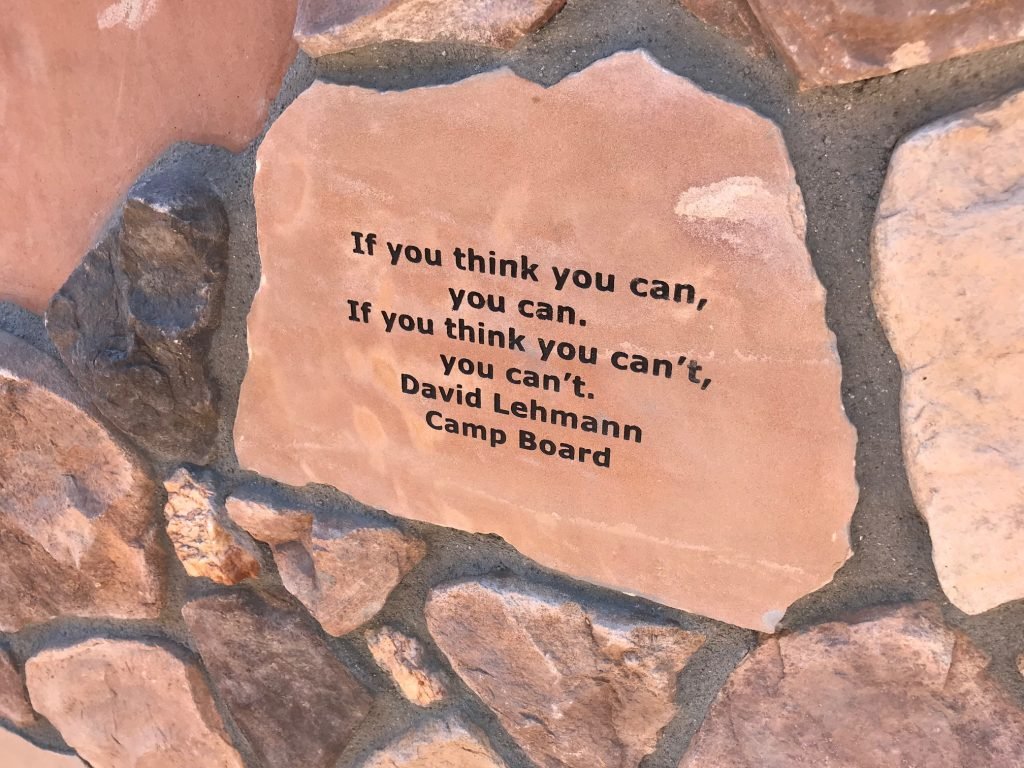 A motivational quote inscribed on a limestone rock surrounded by other stones. The quote reads: 'If you think you can, you can. If you think you can't, you can't.' by David Lehmann, Camp Board.