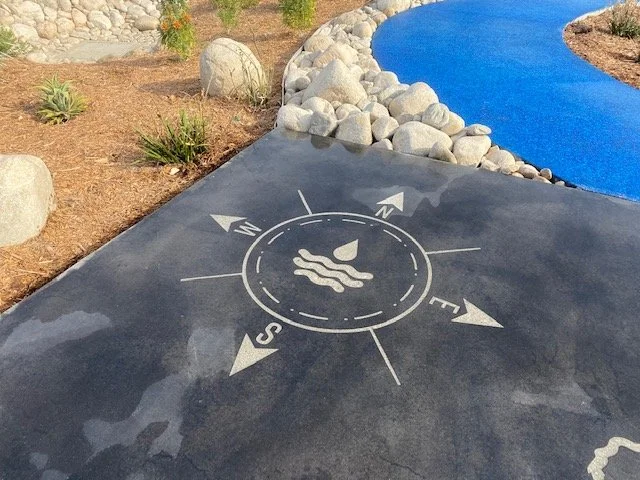 Miniature golf course with a compass rose design and a sailboat in the center on a black asphalt surface.