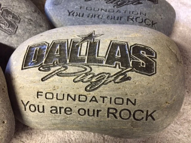 A decorative rock with the words "Dallas Proud Foundation You are our ROCK" engraved on it.