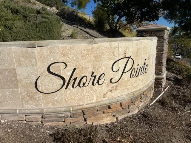 A beige stone wall with the words "Share Pointe" written in black cursive font, located outdoors with trees and a clear blue sky in the background.