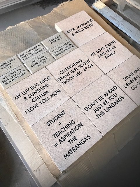 Stack of ceramic tiles with handwritten messages and dedications, including names, family references, and motivational quotes.