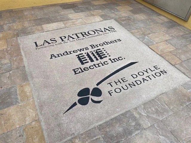 A carpet with logos and text for Las Patronas, Andrews Brothers Electric Inc., and The Doyle Foundation, placed on a tiled floor