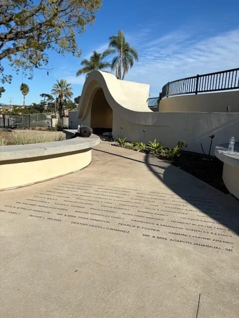 Public park with modern architectural structure, palm trees, and a clear blue sky.