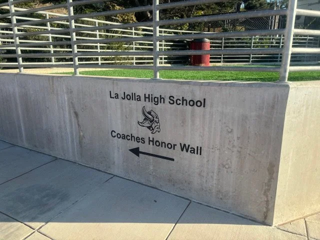 Concrete wall with the text 'La Jolla High School Coaches Honor Wall' and an arrow pointing left, along with a school mascot illustration.