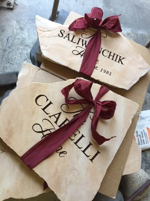 Two paper bags with maroon ribbon bows, labeled "Salivanchik" and "Clavelly," placed on a cardboard box on a concrete surface.