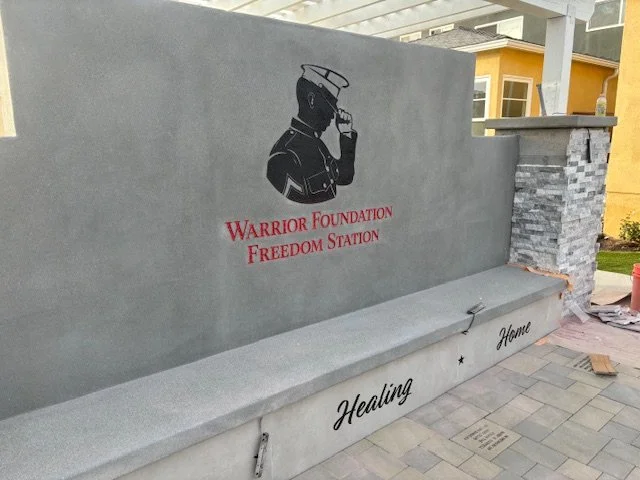 A concrete wall with a silhouette of a soldier and text that reads "Warrior Foundation Freedom Station." There is also a bench with the words "Healing" and "Home" inscribed on it.
