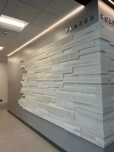 Interior wall with white textured panels displaying engraved names. The top corner shows part of a sign reading 'PARKER' and another partially visible sign.