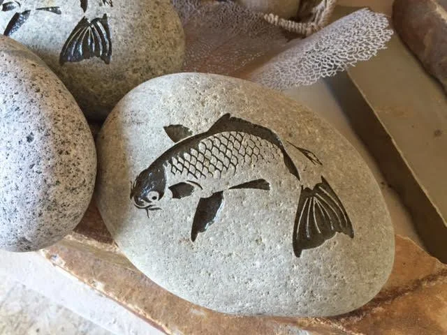 Decorative stone with a black fish and butterfly painted on it.