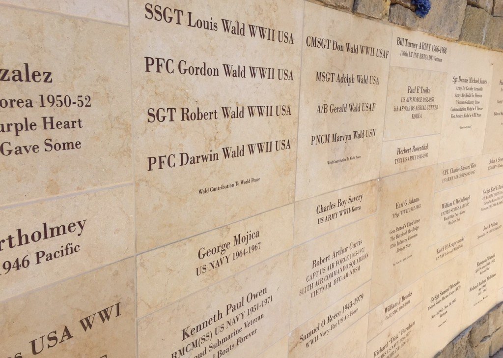 Memorial wall with names of military veterans from WWII, Korea, Vietnam, and WWII, including ranks, service branches, and service years.