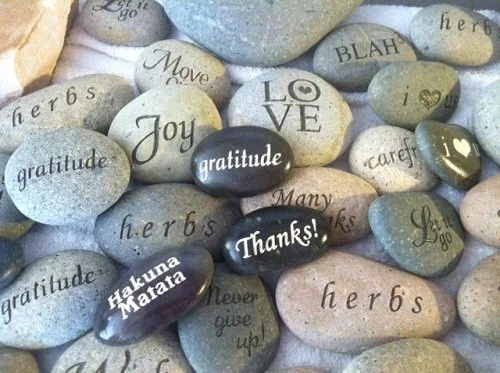 Collection of engraved and painted rocks with words like gratitude, joy, thanks, love, and herbs.