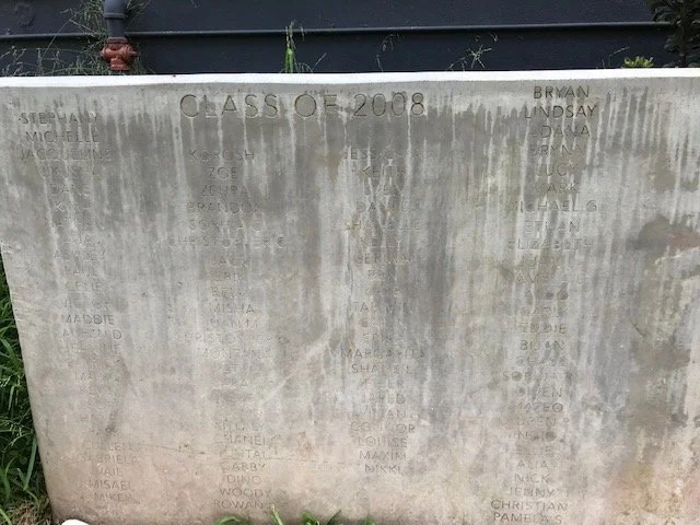 A weathered concrete memorial wall with the words 'Class of 2008' engraved at the top, containing names of individuals etched into the surface.