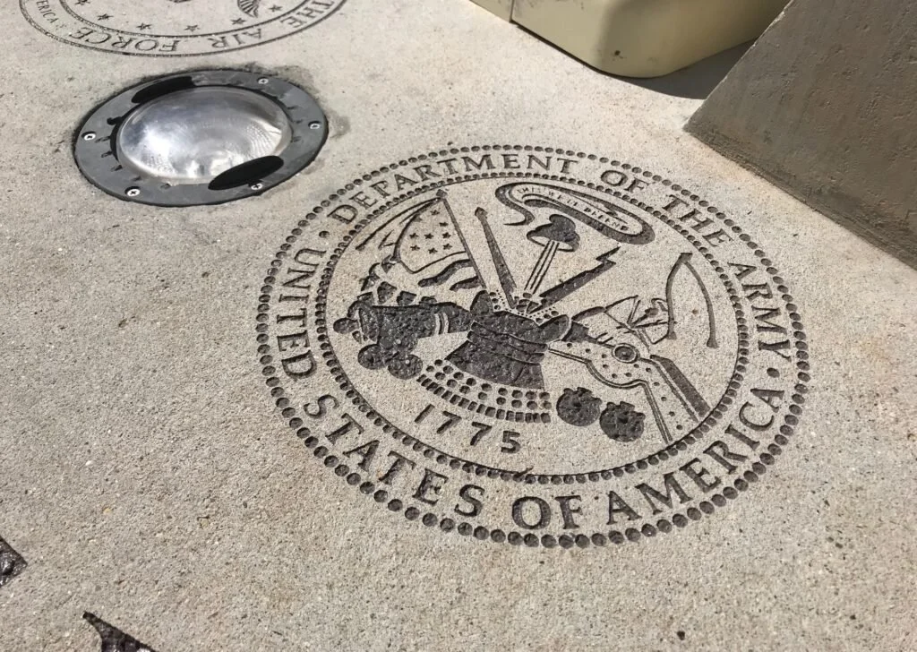 The Great Seal of the United States of America engraved on the sidewalk, featuring an eagle holding olive branch and arrows, with a shield on its chest, and the text "United States of America" and "Department of the Army" surrounding it.