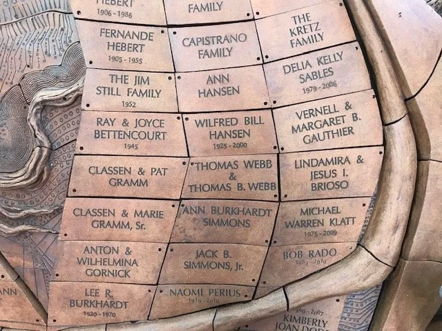 Close-up of a memorial wall with engraved names and birth-death years, arranged in rows with a curved stone border.