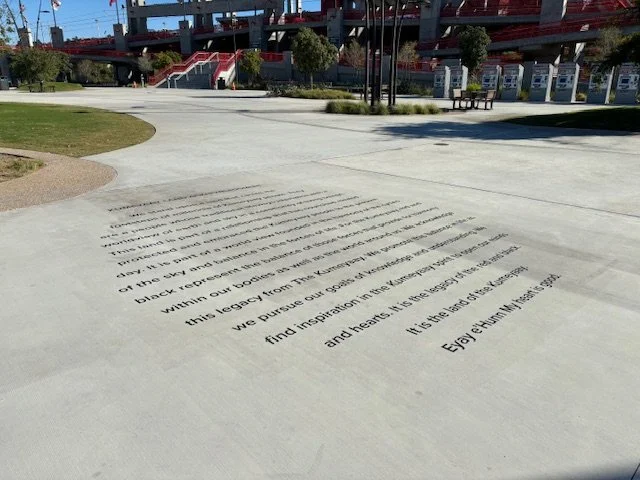 Concrete ground with text engraved into it, outdoors with parked cars and a nearby walking area.