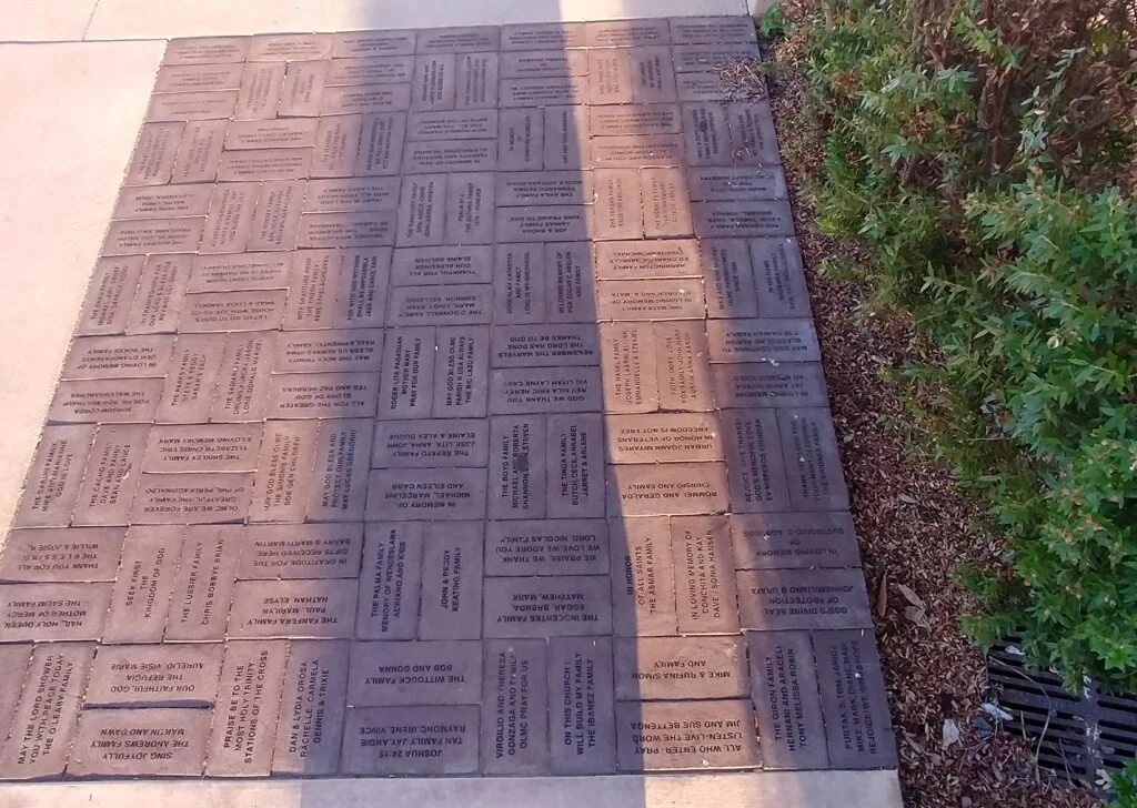 A memorial sidewalk with engraved bricks honoring fallen soldiers, located next to a sidewalk and a green shrub.