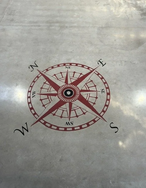 A compass rose painted on concrete floor showing directions N, E, S, W, and diagonals NE, SE, NW, SW.