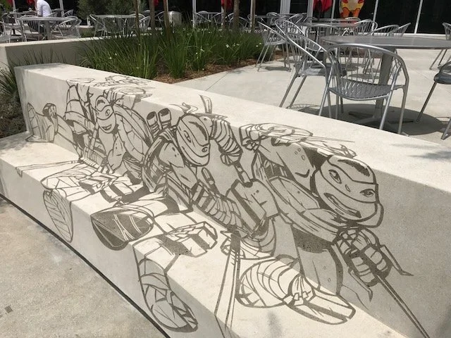 Black and white mural of cartoon turtles with weapons on a concrete bench in an outdoor seating area.