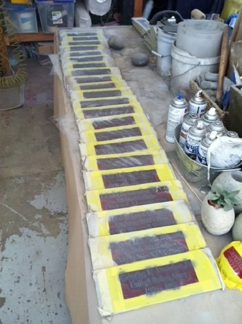 Multiple headstones with yellow borders lined up on a workbench in a workshop.