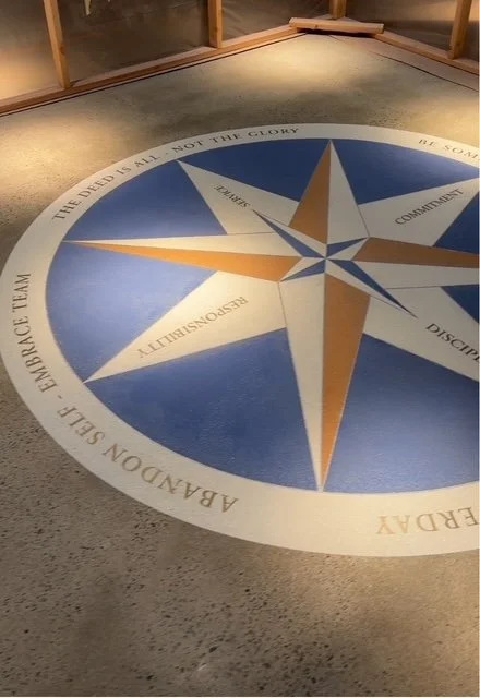Compass rose floor design with various words and phrases in a circle, including 'ABANDON SELF', 'HARDACE TEAM', and others, in an indoor setting.