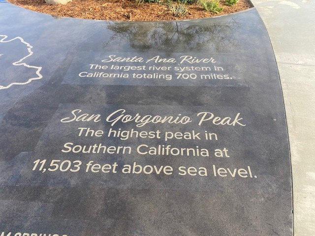 A concrete or stone surface with engraved text about the Santa Ana River and San Gorgonio Peak, including their geographic details.