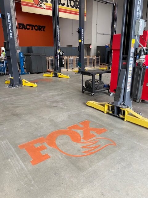 A concrete floor with an orange Fox logo painted on it in front of two vehicle lifts in an auto repair shop.