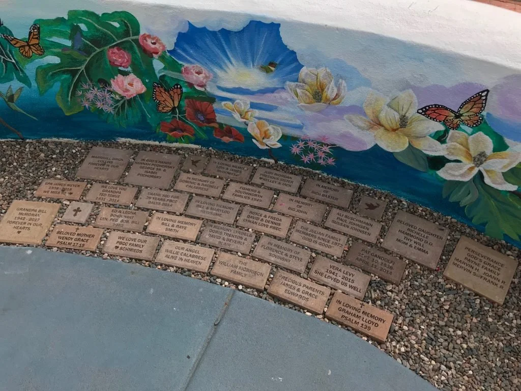Murals of flowers and butterflies above a memorial walk with engraved bricks honoring loved ones.
