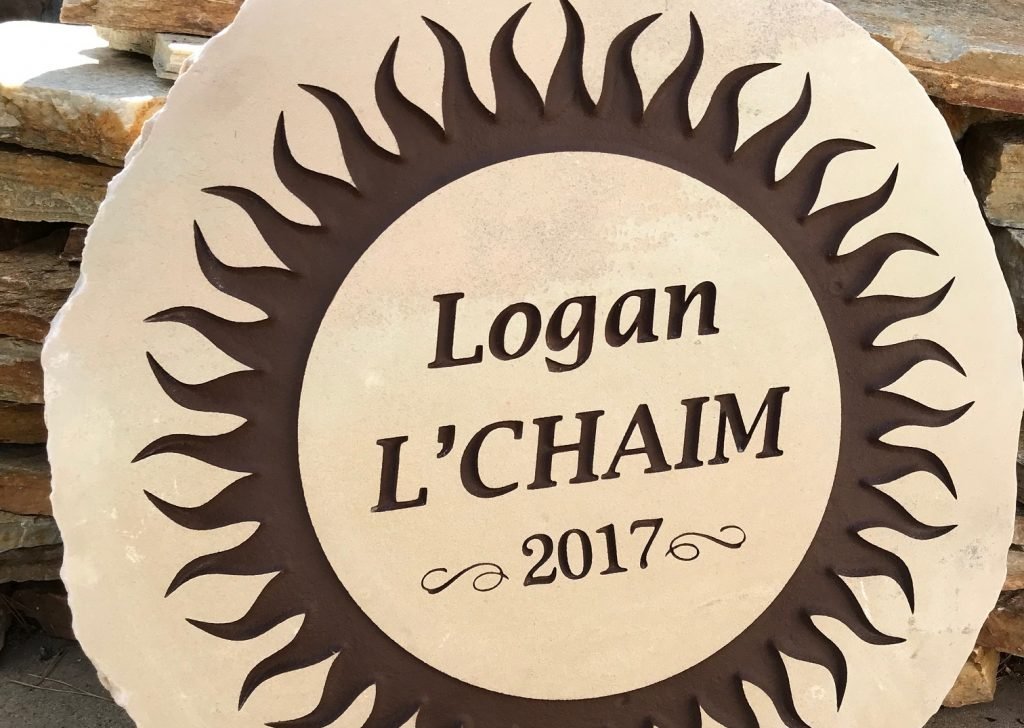 A circular stone sign with a decorative sunburst pattern around the edge, inscribed with the text 'Logan L'CHAIM 2017'.