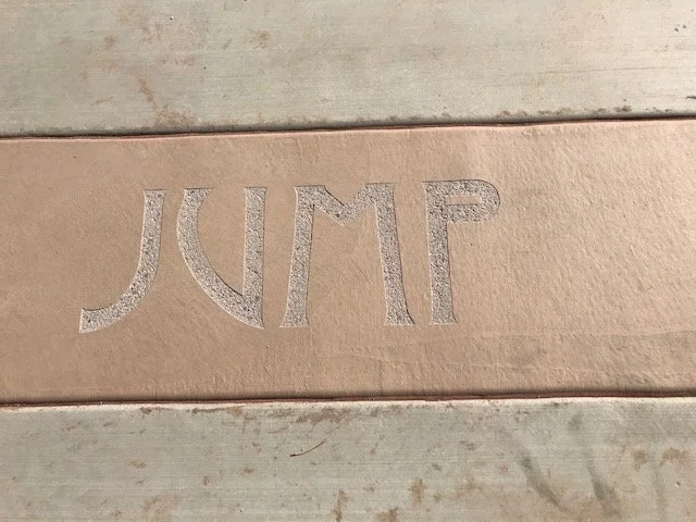 Close-up of the word 'JUMP' engraved on a wooden surface.