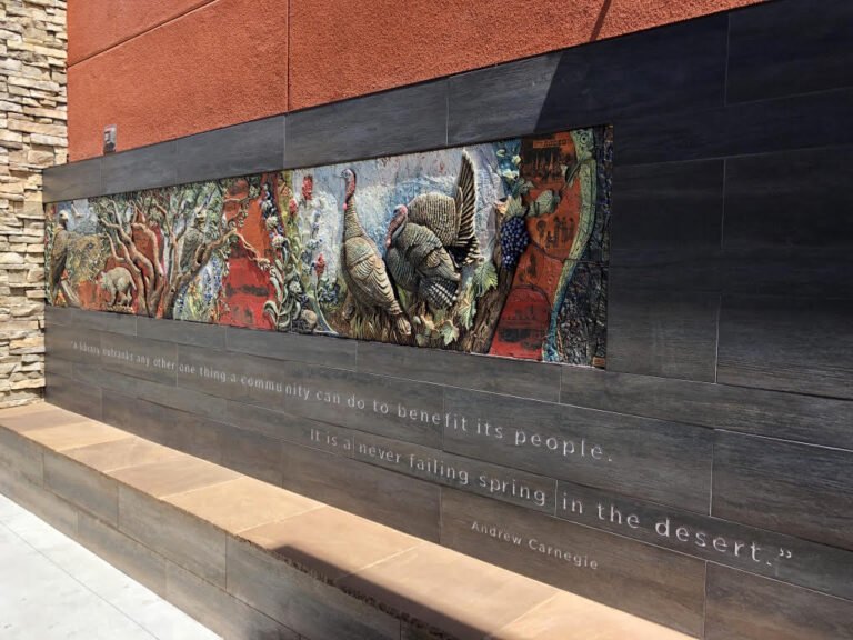 A colorful mural with turkeys and nature scenes, mounted on a dark wooden wall with an engraved quote about community and spring.