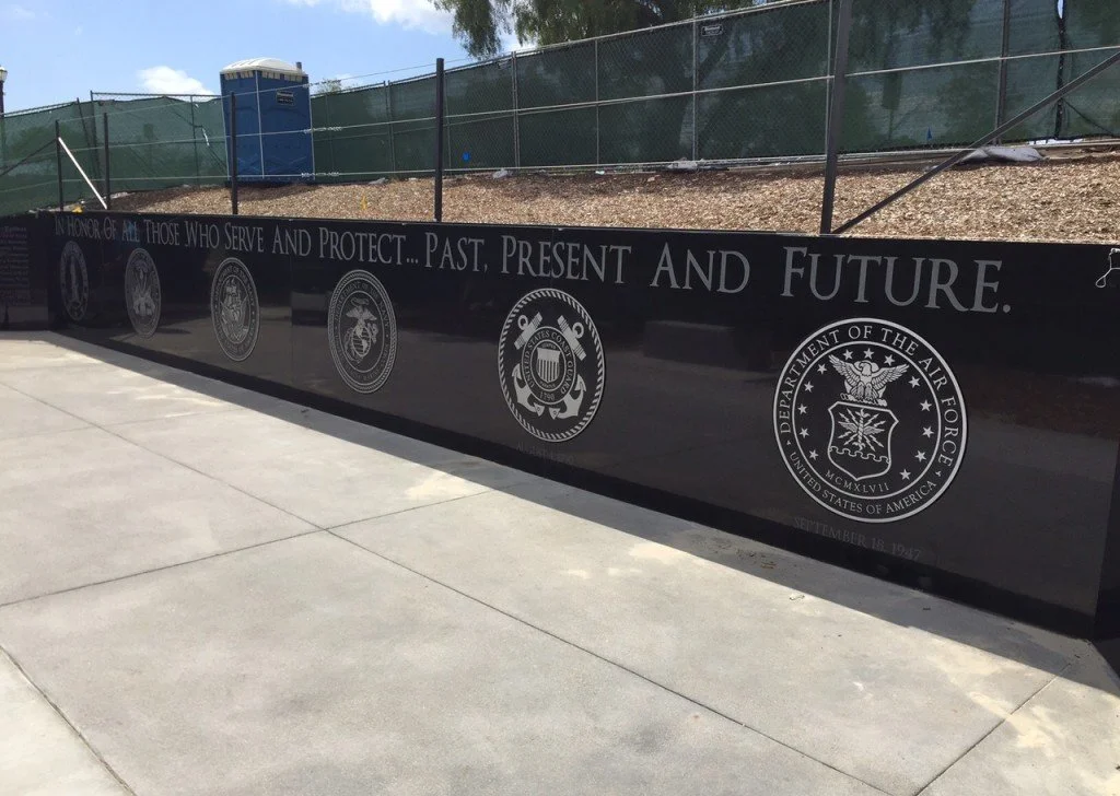 Black memorial wall displaying the phrase 'In Honor of All Those Who Serve and Protect... Past, Present, and Future', with multiple military and government seals, including the U.S. Department of the Air Force emblem.