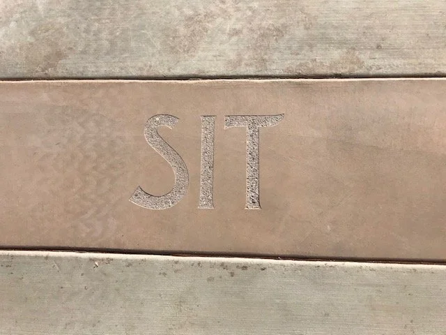 Close-up of the word 'SIT' engraved in a wooden surface.