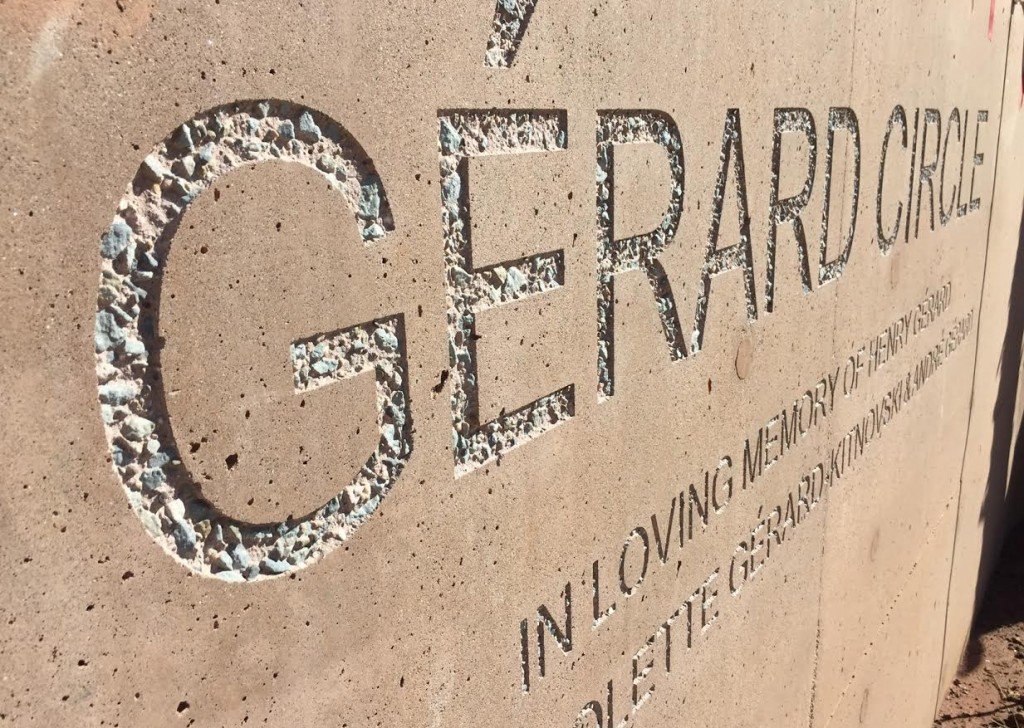 Close-up of engraved text on a concrete memorial plaque, reading "GERARD CIRCLE" and a partial phrase, in loving memory of the many lives lost.