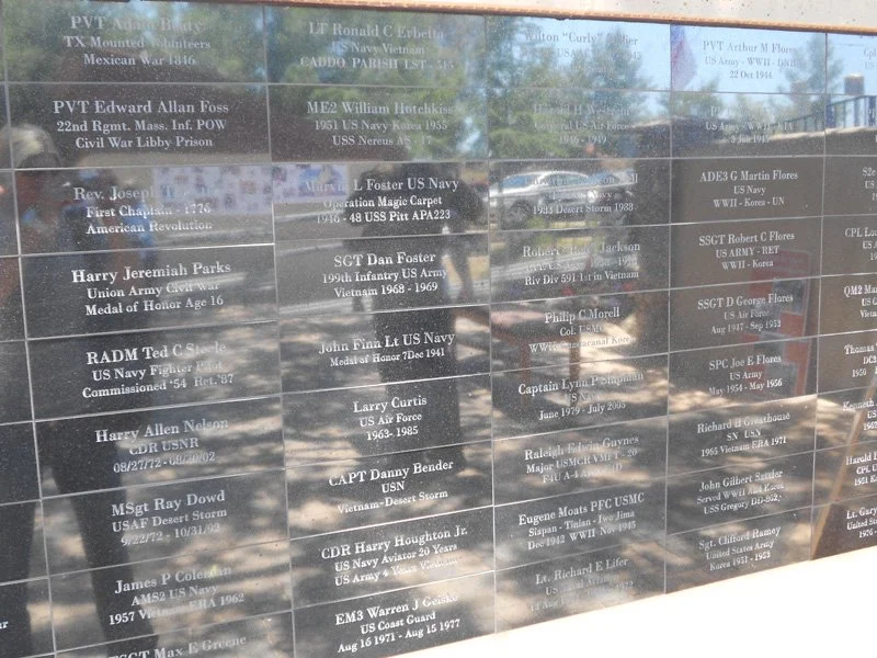 A memorial wall with names and details of military servicemen and women engraved on dark marble plaques.