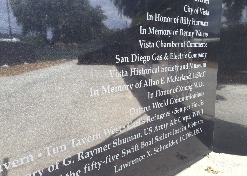 A black monument or plaque with engraved white text honoring multiple individuals and organizations, including Billy Harmatz, Denny Waters, Allan E. McFarland, Xuong N. Du, and G. Raymer Shuman, and mentioning the Vista Historical Society, San Diego 