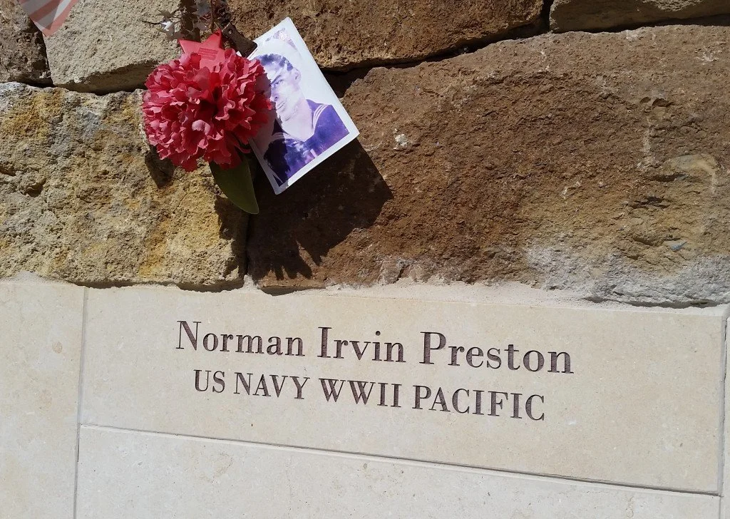 A memorial plaque for Norman Irvin Preston, US Navy WWII Pacific, with a pink flower and a black-and-white photograph of a young man attached above the plaque.