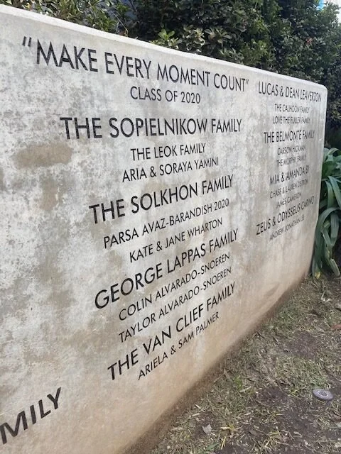 A memorial wall with engraved text honoring families and individuals, including the class of 2020 and various family names.